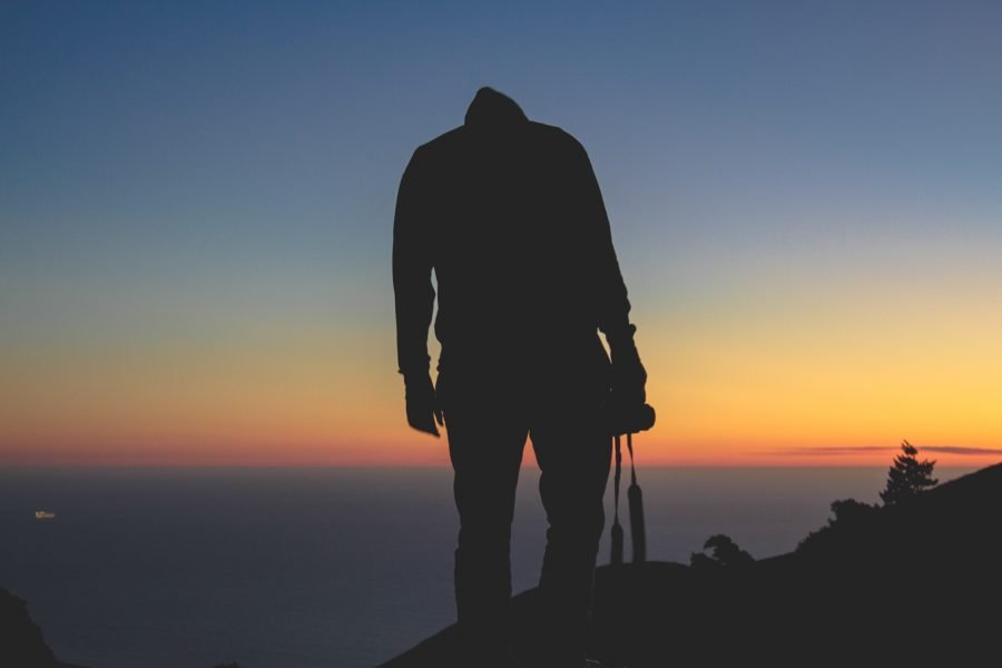 imagem ilustrativa de um fotógrafo em contra-luz no pôr-do-sol de cabeça baixa para representar o que pensar antes de fotografar