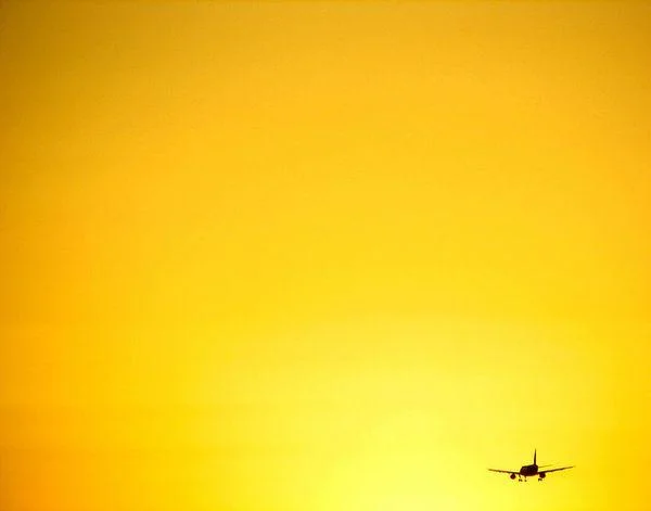 exemplo de foto minimalista de céu todo amarelo e um detalhe de avião em contraluz no canto inferior direito