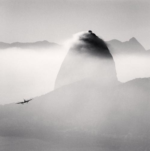 exemplo de fotografia minimalista de avião, nuvens e uma pedra ao fundo, em preto e branco