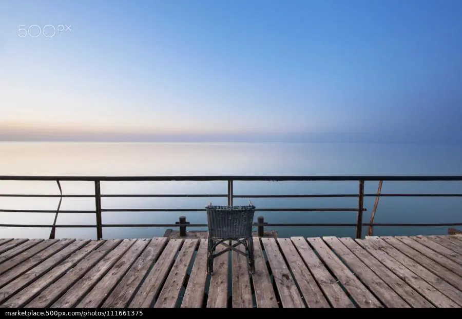 foto minimalista de um pier de madeira, um oceano e céu azul e um cadeira vazia