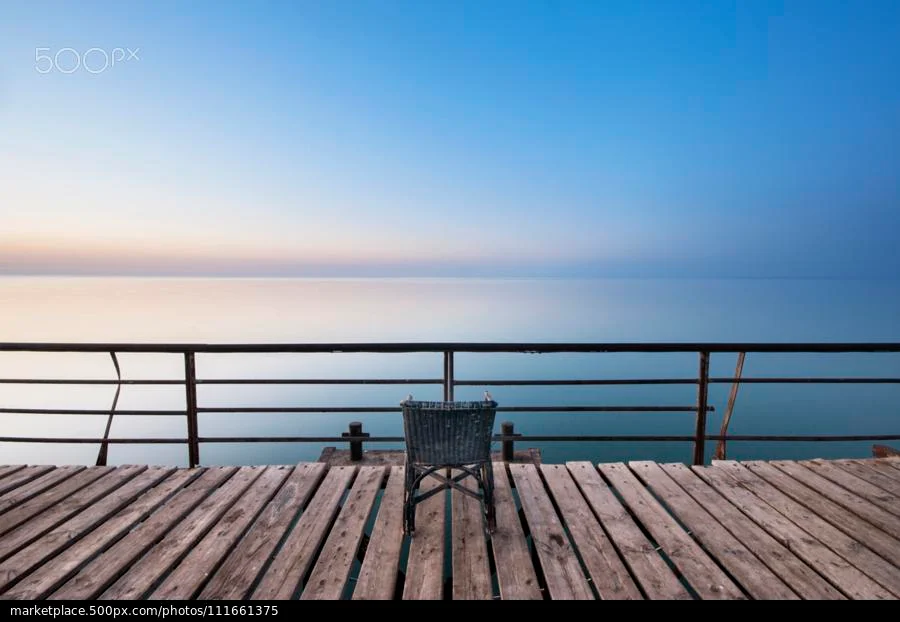 foto minimalista de um pier de madeira, um oceano e céu azul e um cadeira vazia