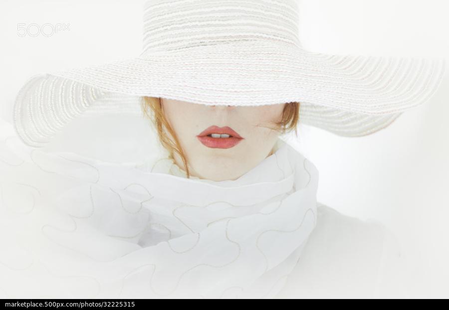 minimalismo na fotografia de uma mulher usando um grande chapéu e cores de roupa, e fundo predominante branco, com destaque na boca vermelha