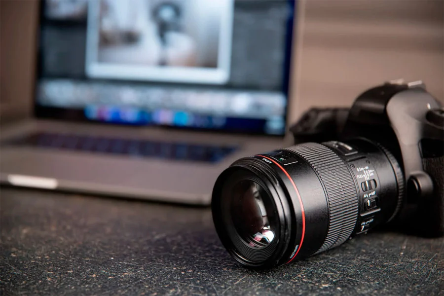 câmera sobre a mesa com computador desfocado no fundo - cursos de fotografia online