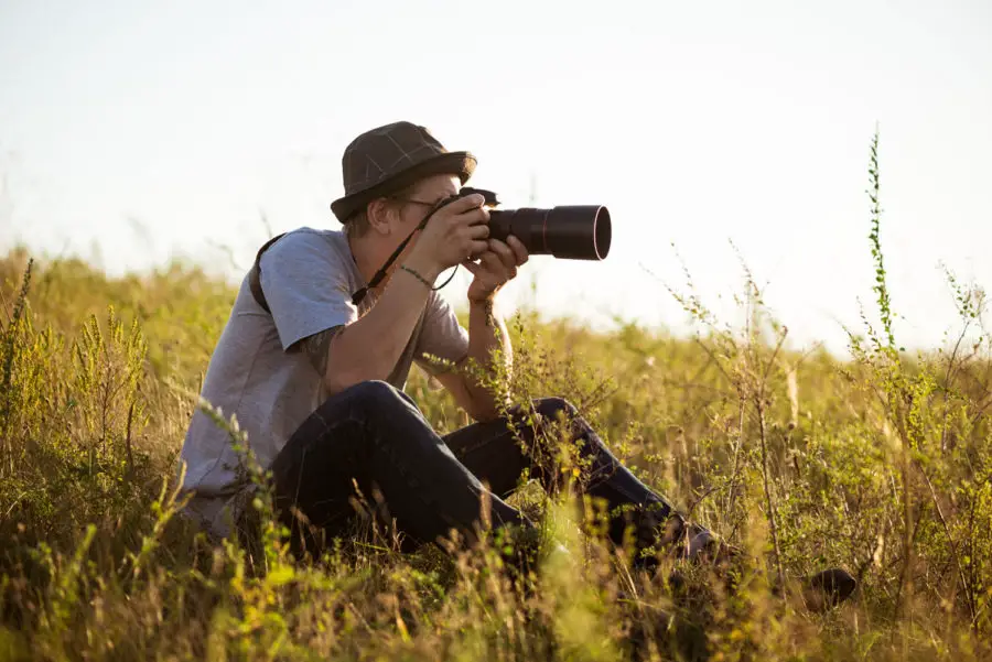 homem com câmera sentado no meio do mato - dicas para iniciar sua carreira como fotógrafo